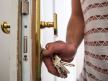 Muška ruka koja drži ključ i otključava/zaključava ulazna vrata od kuće.