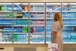 Žena u supermarketu stoji ispred frižidera sa vodom i drugim pićima