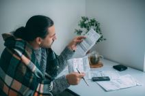 muškarac ogrnut ćebetom gleda račune za struju i grejanje