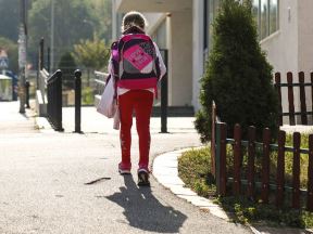 Devojčica sa rancem na leđima ispred škole