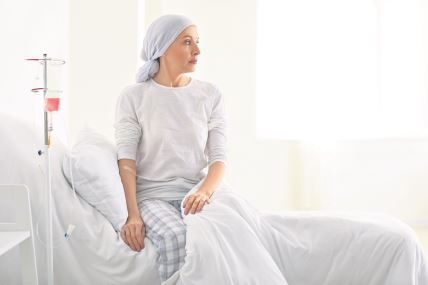 Žena sedi na krevetu, s turbanom na glavi, prima hemoterapiju – bori se protiv raka.