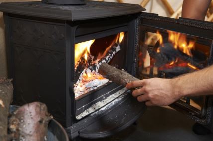 muškarac ubacuje u peć parče drveta