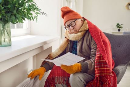 muškarac umotan u ćebe sedi pored radijatora