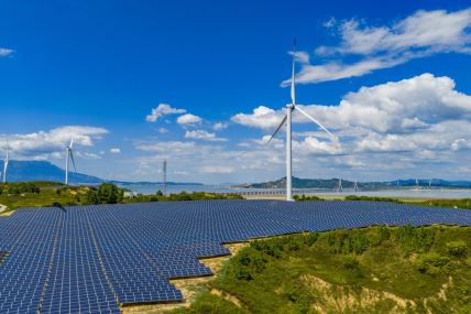 solarna elektrana postavljena na zemlji dok se u pozadini vidi vetropark