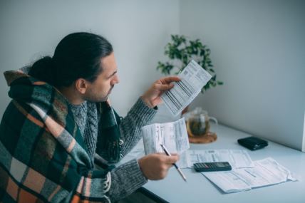 muškarac ogrnut ćebetom gleda račune za struju i grejanje