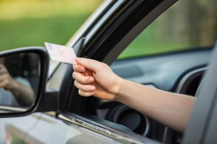 vozač pokazuje vozačku dozvolu kroz prozor automobila