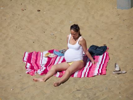 trudnica sedi na peškiru na plaži