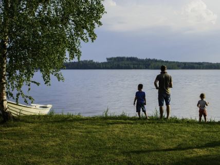 Otac sa dvoje dece peca na obali jezera pored belog čamca u Finskoj.