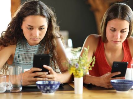 Dve mlade devojke gledaju u telefone.