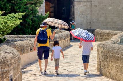 Otac sa dvoje dece šeta u Italiji i drži kišobran u ruci kako bi se zaštitili od vrućine