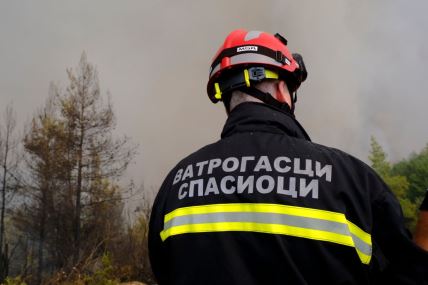 Muškarac na čijoj jakni piše 'vatrogasci spasioci' učestvuje u gašenju požara na grčkom ostrvu Evija