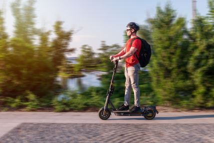 Muškarac se vozi na električnom trotinetu, a nosi i zaštitnu kacigu i ranac