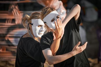 Dve žene sa maskama na licu plešu tokom predstave na otvorenom
