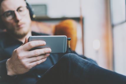 muškarac sa slušalicama gleda snimke na mobilnom telefonu