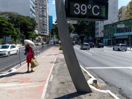 Žena se štiti od vrućine u Brazilu dok je na ekranu ispisano da je temperatura 39 stepeni