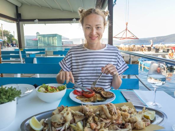 Devojka uziva u lokalnoj hrvatskoj kuhinji u restoranu kraj mora