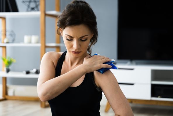 devojka u crnoj majci na bretele drži desnom rukom hladnu oblogu na levom ramenu