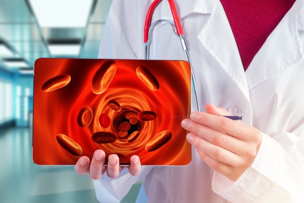 medicinski radnik u belom mantilu drži papir na kom su prikazana crvena krvna zrnca