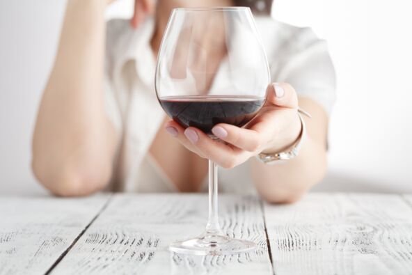 žena drži čašu sa crvenim vinom na drvenom stolu