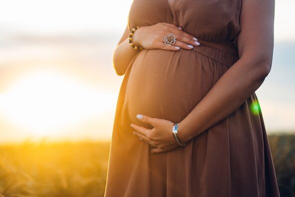 trudna žena u prirodi miluje stomak, u pozadini zalazak sunca
