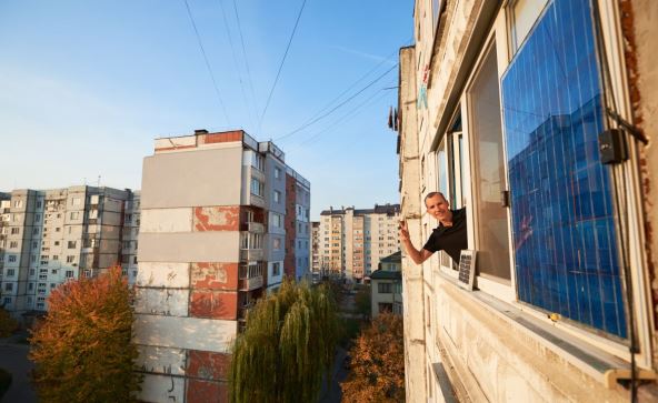 Čovek maše sa prozora dok su na zidu zgrade postavljeni solarni paneli