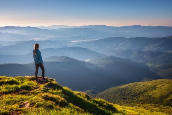 Žena stoji na vrhu planine i gleda obronke