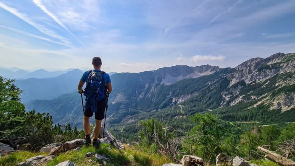 Planinar stoji na vrhu planine na granici Slovenije i Austrije i divi se pogledu